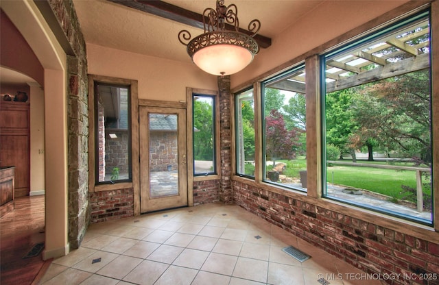 unfurnished sunroom with visible vents, tile patterned flooring, and brick wall