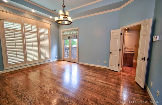 spare room featuring an inviting chandelier, ornamental molding, baseboards, and wood finished floors