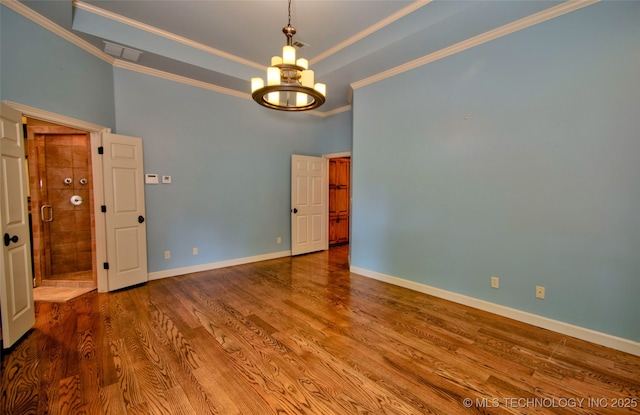 spare room with crown molding, a notable chandelier, baseboards, wood finished floors, and visible vents