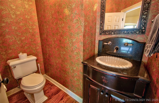 bathroom with baseboards, toilet, wallpapered walls, and wood finished floors