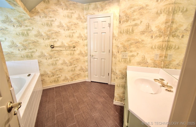 bathroom with baseboards, vanity, tiled bath, and wallpapered walls