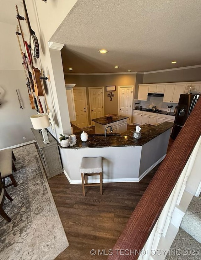 kitchen featuring ornamental molding, dark countertops, a textured ceiling, under cabinet range hood, and black fridge