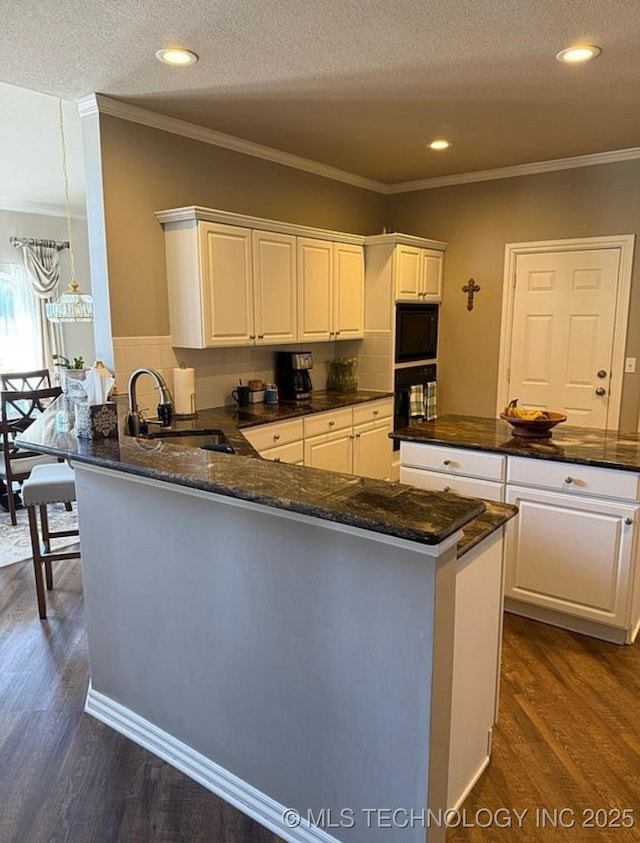 kitchen featuring a peninsula, dark wood finished floors, ornamental molding, and a sink
