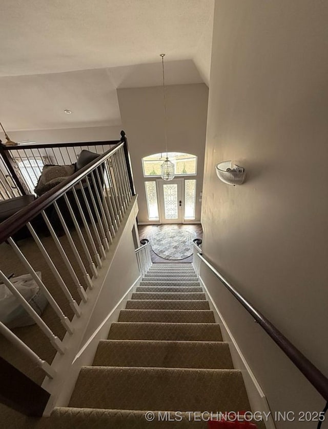 stairs with carpet floors, high vaulted ceiling, and a chandelier