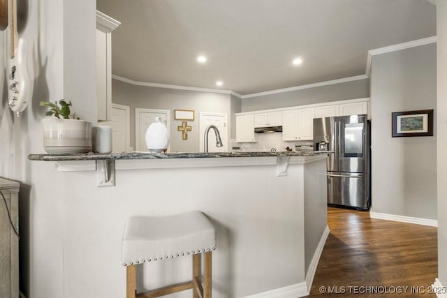 3401 N Narcissus Ave, Broken Arrow, OK 74012 - kitchen featuring stainless steel refrigerator with ice dispenser, a breakfast bar, dark stone counters, under cabinet range hood, and ornamental molding