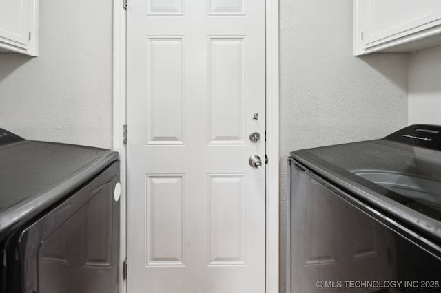 washroom with a textured wall, cabinet space, and washer and clothes dryer