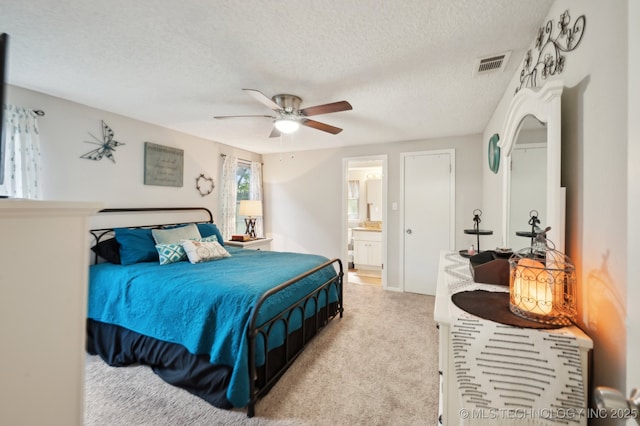 bedroom with visible vents, connected bathroom, a textured ceiling, and light carpet