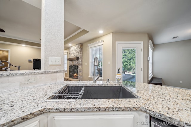 kitchen with visible vents, crown molding, a fireplace, light stone counters, and a sink