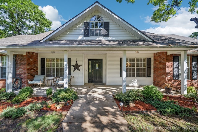view of front of property featuring a porch, a shingled roof, and brick siding