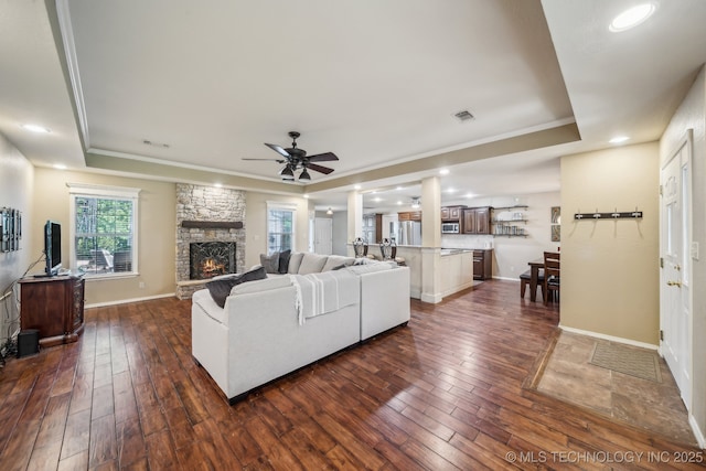 living area featuring dark wood-type flooring, a ceiling fan, a raised ceiling, and ornamental molding