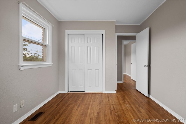 unfurnished bedroom featuring visible vents, baseboards, wood finished floors, and a closet
