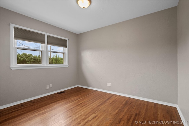 spare room featuring baseboards, wood finished floors, and visible vents