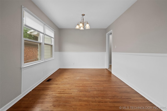 spare room with a chandelier, baseboards, visible vents, and wood finished floors