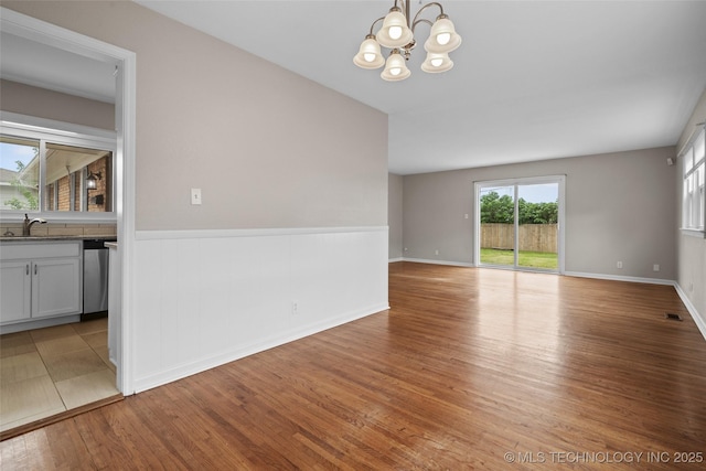 spare room featuring wainscoting, a sink, light wood finished floors, a chandelier, and visible vents