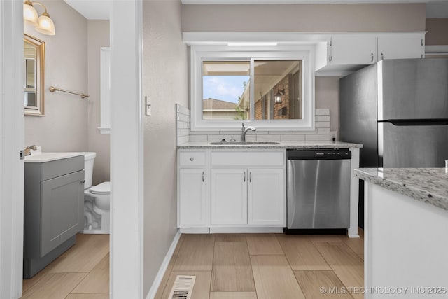 kitchen featuring light stone countertops, appliances with stainless steel finishes, a sink, white cabinetry, and baseboards