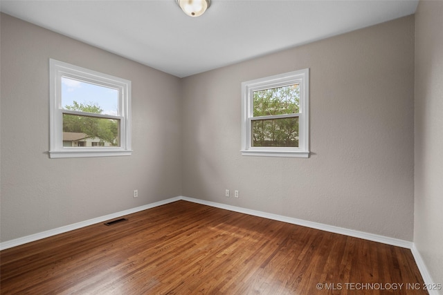 unfurnished room with baseboards, wood finished floors, and visible vents
