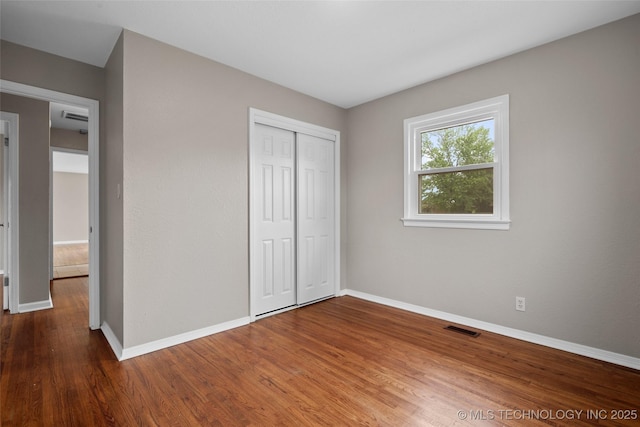 unfurnished bedroom with baseboards, visible vents, wood finished floors, and a closet