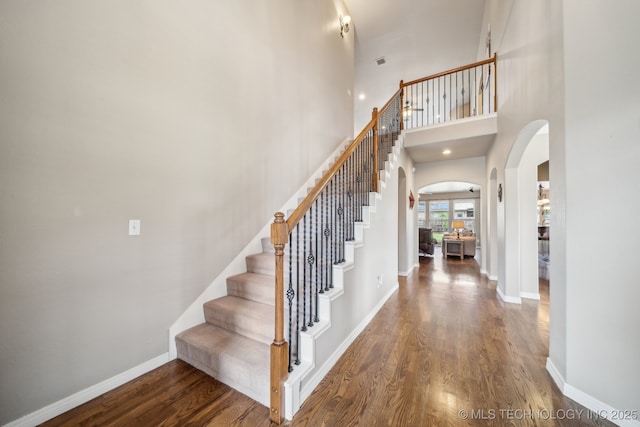 stairway with baseboards, arched walkways, wood finished floors, and visible vents