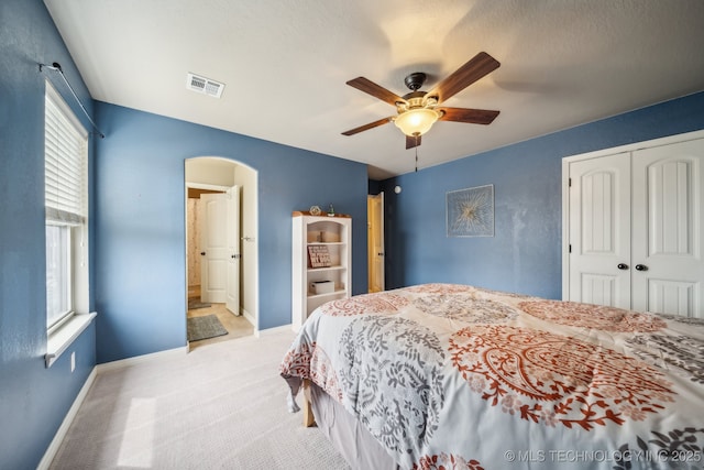 carpeted bedroom featuring arched walkways, visible vents, multiple windows, and a closet