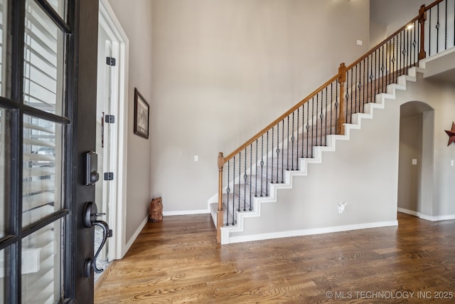 entrance foyer with stairs, wood finished floors, baseboards, a high ceiling, and arched walkways