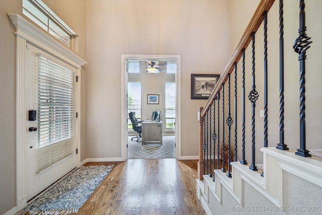foyer entrance with ceiling fan, wood finished floors, baseboards, a high ceiling, and stairs