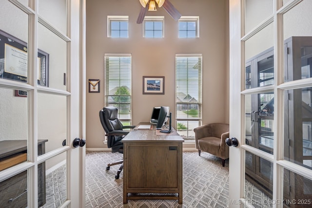 carpeted office featuring french doors, a ceiling fan, a towering ceiling, and a wealth of natural light