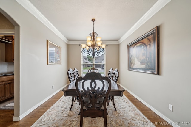 dining space with crown molding, arched walkways, dark wood finished floors, baseboards, and an inviting chandelier