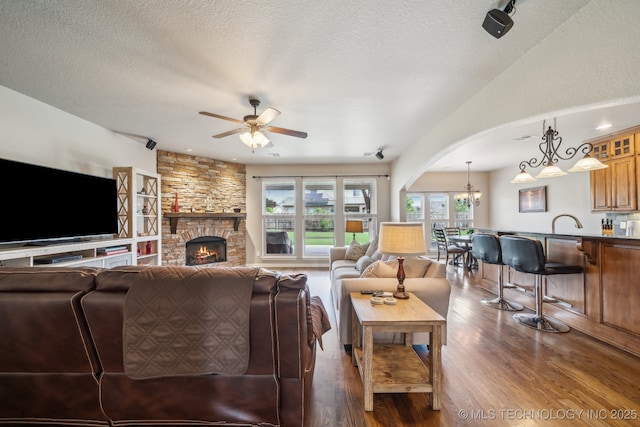 living room featuring arched walkways, a textured ceiling, ceiling fan with notable chandelier, and dark wood-style floors