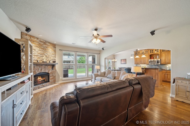 living area with arched walkways, light wood-style flooring, a ceiling fan, and a textured ceiling