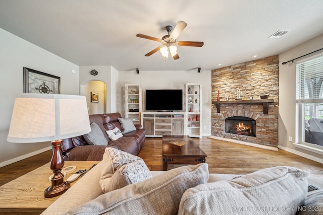 living room with wood finished floors, a fireplace, baseboards, ceiling fan, and arched walkways