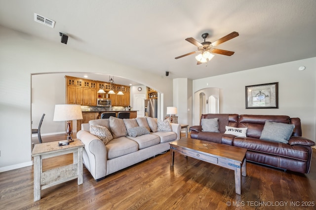 living area with arched walkways, a ceiling fan, baseboards, wood finished floors, and visible vents