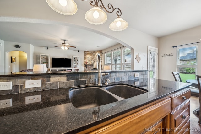 kitchen featuring open floor plan, arched walkways, brown cabinets, a sink, and dark stone countertops