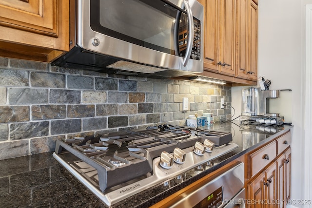 kitchen with decorative backsplash, stainless steel appliances, brown cabinetry, and dark stone countertops