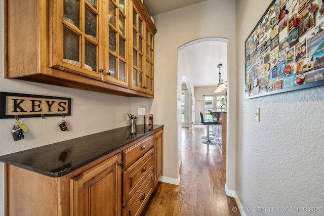 bar with a bar, arched walkways, dark wood-style flooring, and baseboards