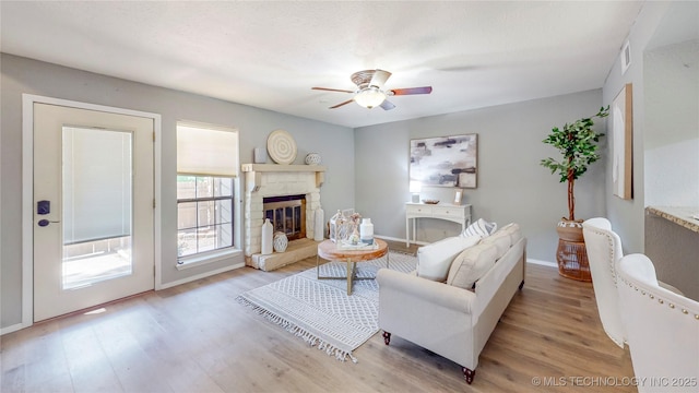 living area with baseboards, ceiling fan, wood finished floors, and a fireplace