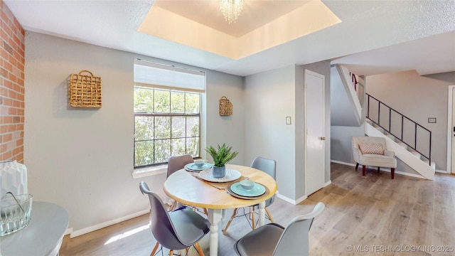 dining space featuring light wood-type flooring, a raised ceiling, baseboards, and stairway
