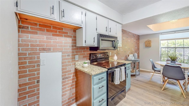 kitchen with light stone countertops, baseboards, light wood-type flooring, a skylight, and black appliances
