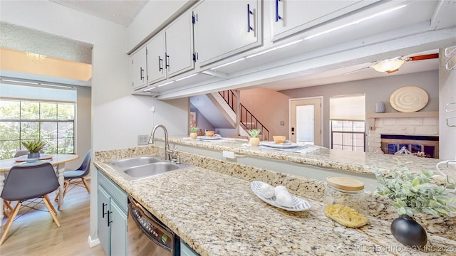kitchen with white cabinets, a sink, a glass covered fireplace, light wood-type flooring, and stainless steel dishwasher