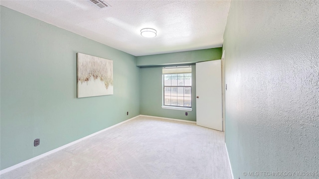 carpeted spare room featuring baseboards, a textured ceiling, and visible vents