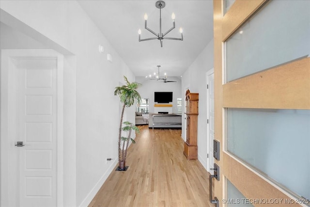 hall featuring baseboards, an inviting chandelier, and light wood-style floors