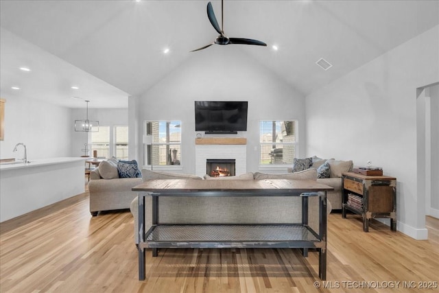 living room with light wood-style floors, ceiling fan, a wealth of natural light, and a lit fireplace