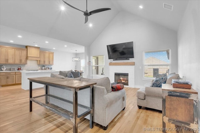 living room with a fireplace, light wood-style floors, ceiling fan, high vaulted ceiling, and recessed lighting