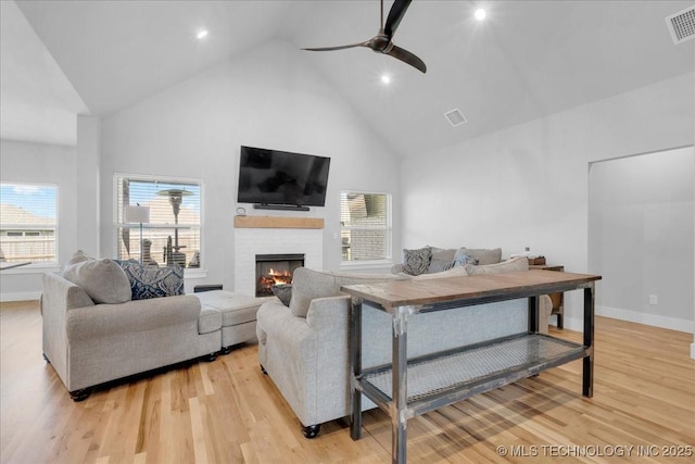 living area with high vaulted ceiling, ceiling fan, a fireplace, and light wood-style flooring