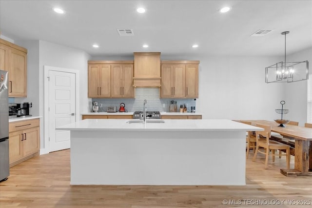kitchen featuring light brown cabinetry, custom range hood, and visible vents
