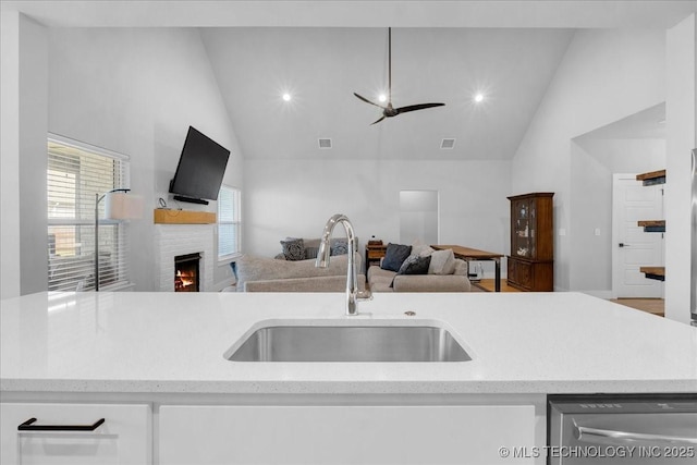kitchen featuring a sink, dishwasher, high vaulted ceiling, open floor plan, and a lit fireplace