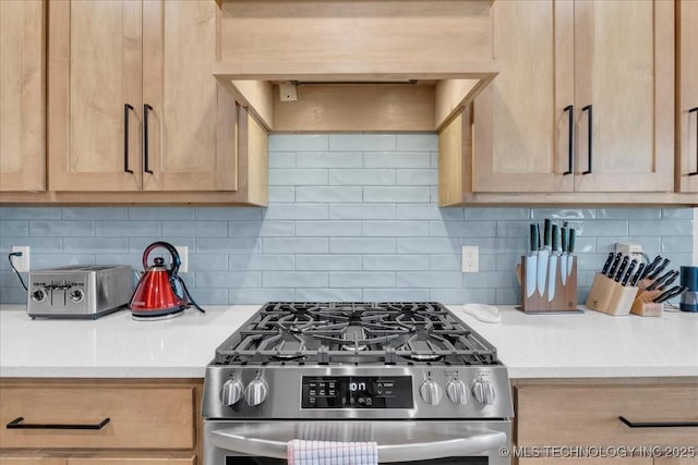 kitchen with light brown cabinets, stainless steel gas range oven, light countertops, tasteful backsplash, and custom range hood