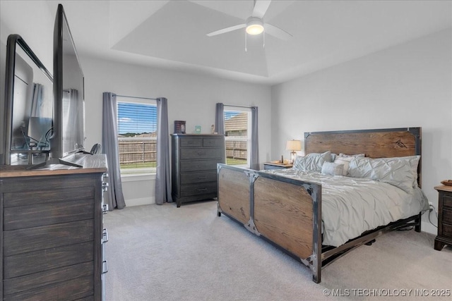 bedroom featuring ceiling fan, light colored carpet, baseboards, and a tray ceiling