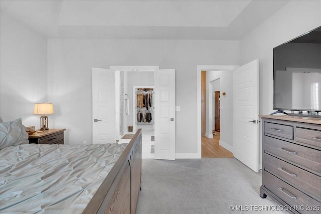 carpeted bedroom featuring baseboards, a raised ceiling, and a spacious closet