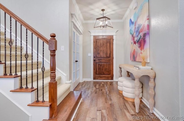 foyer entrance with crown molding, wood finished floors, stairway, baseboards, and a chandelier