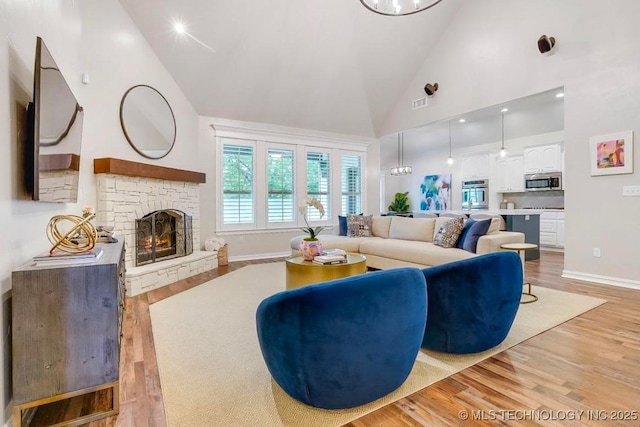 living room with visible vents, a fireplace, high vaulted ceiling, baseboards, and light wood-style flooring